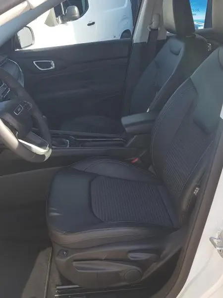 Vue intérieure côté conducteur du Jeep Compass blanc 2024, sièges noirs avec accoudoir central et commandes visibles.