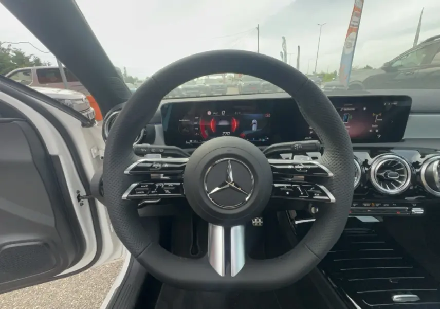 Vue intérieure centrée sur le volant cuir multifonctions noir de la Mercedes Classe A 200D BVA Exclusive Design blanche.