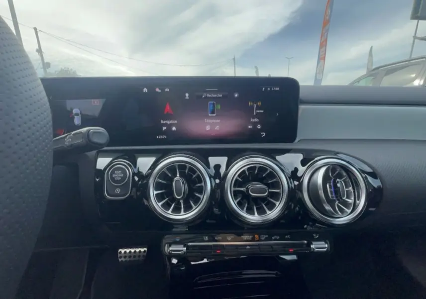 Vue intérieure centrée sur la planche de bord noire et les trois aérateurs ronds chromés d’une Mercedes Classe A blanche polaire.