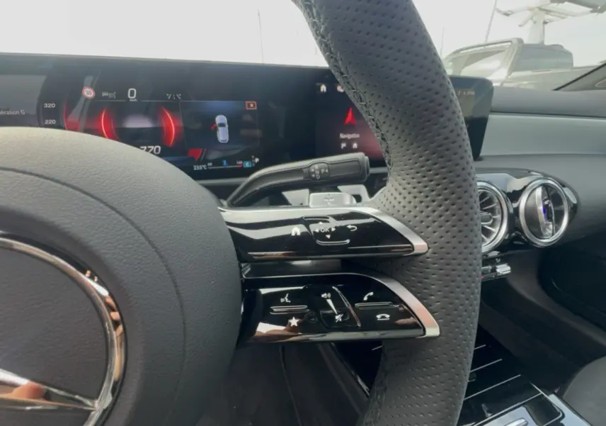 Gros plan sur le volant cuir perforé et les commandes multifonctions du tableau de bord de la Mercedes Classe A blanche.