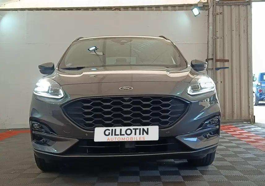 Vue frontale d'un Ford Kuga gris foncé 2023 avec phares LED allumés et calandre noire hexagonale.