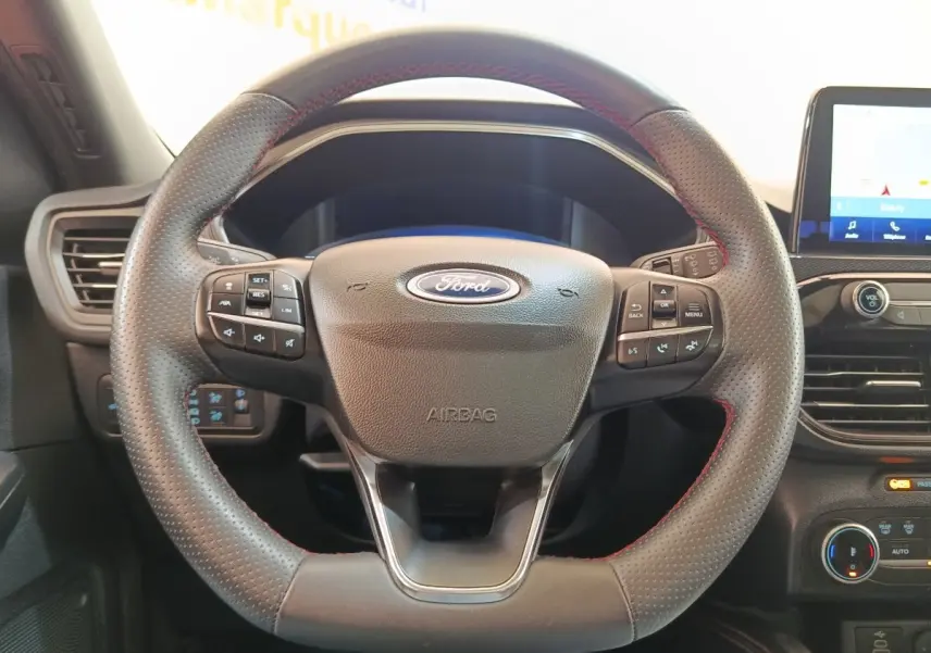 Vue rapprochée du volant cuir noir avec surpiqûres rouges du Ford Kuga gris foncé, tableau de bord et écran tactile visibles.