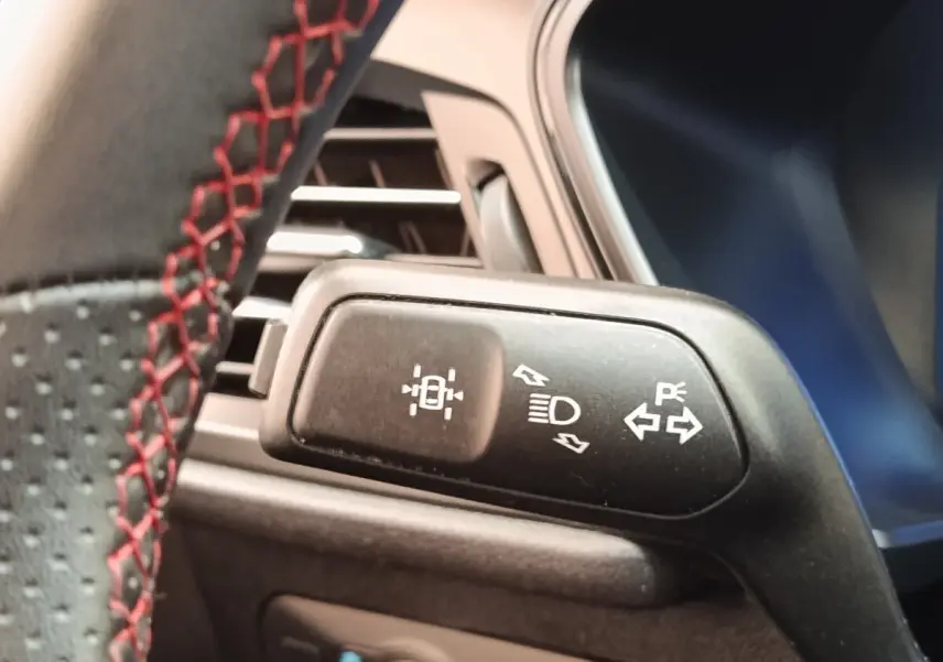 Détail du commodo de phares et clignotants sur le volant avec surpiqûres rouges, intérieur Ford Kuga gris foncé.