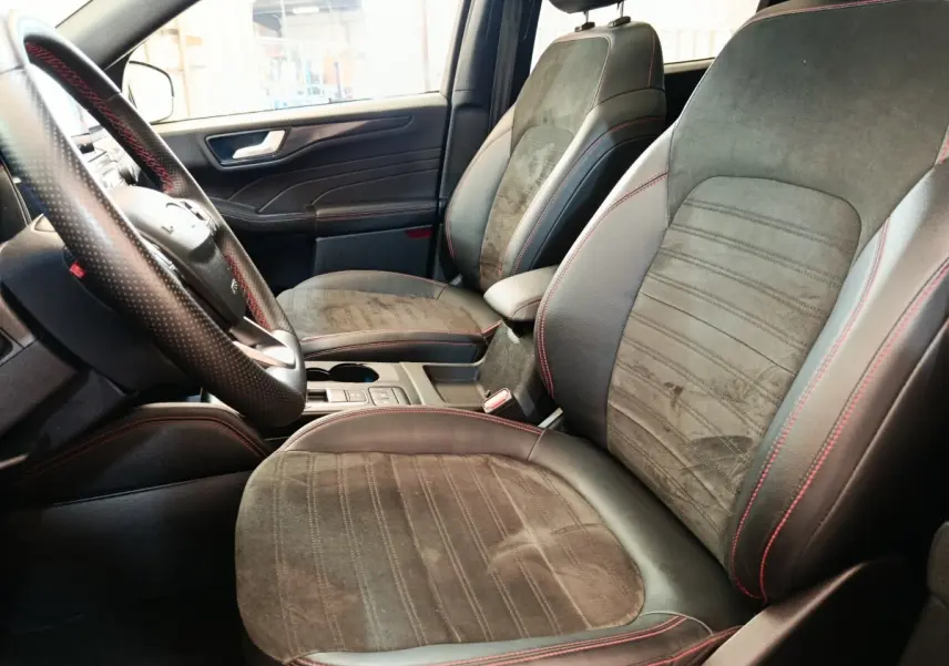 Vue intérieure côté conducteur du Ford Kuga 2023, sièges en cuir et alcantara gris foncé avec surpiqûres rouges.