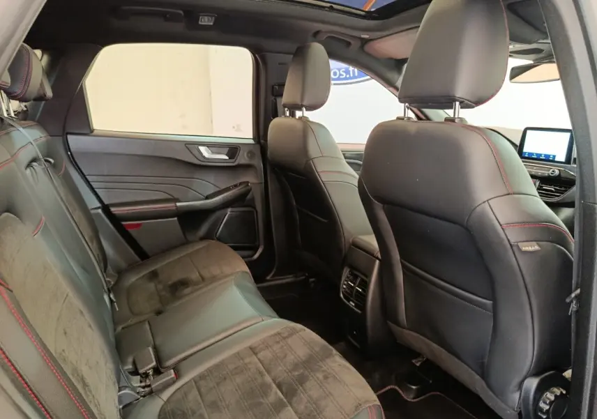 Vue intérieure arrière droite du Ford Kuga 2023, sièges noirs avec surpiqûres rouges et toit ouvrant panoramique.