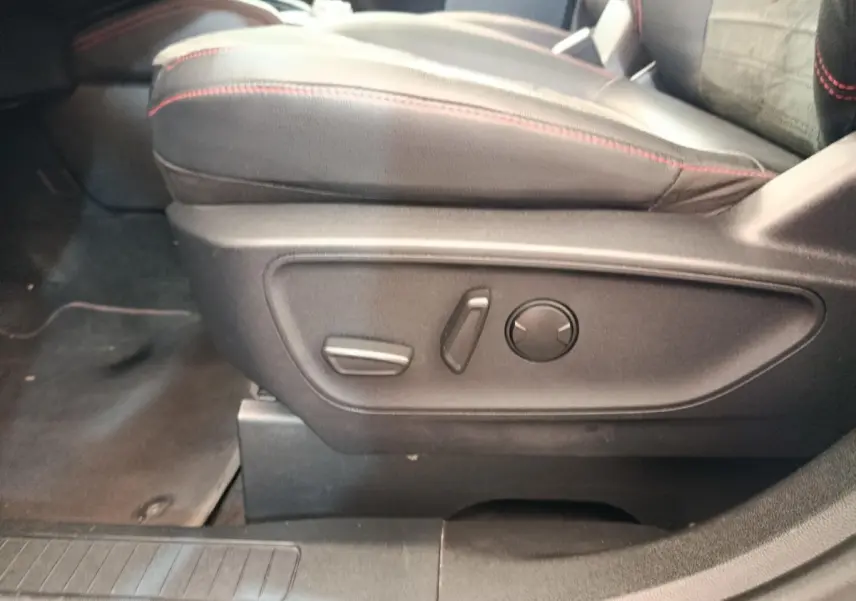 Détail des commandes électriques du siège avant droit en cuir noir avec surpiqûres rouges dans un Ford Kuga gris foncé 2023.