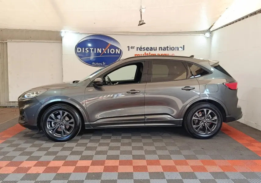 Vue de profil côté gauche d’un Ford Kuga gris foncé ST-Line X avec jantes noires dans un showroom intérieur.