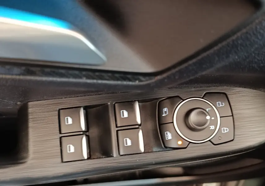 Gros plan sur les commandes de lève-vitres et rétroviseurs côté conducteur du Ford Kuga gris foncé 2023.