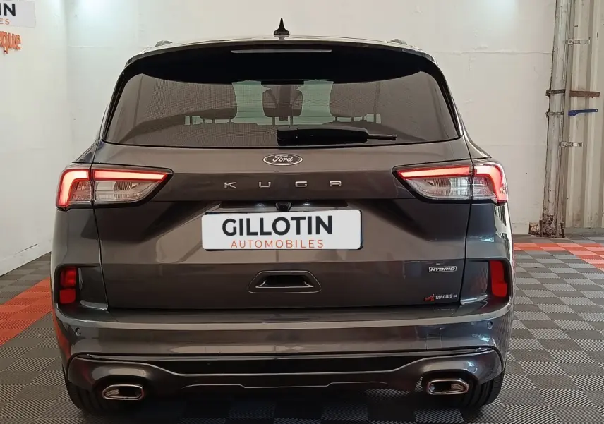 Vue arrière d’un Ford Kuga gris foncé 2023 avec feux LED allumés et double sortie d’échappement rectangulaire.