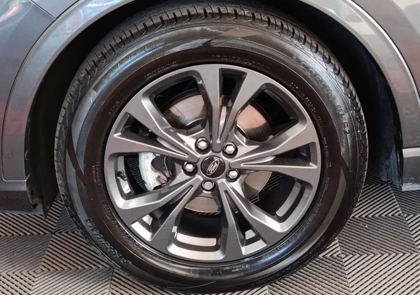Gros plan sur la roue avant droite gris foncé du Ford Kuga 2023 avec jante alliage et logo Ford au centre.
