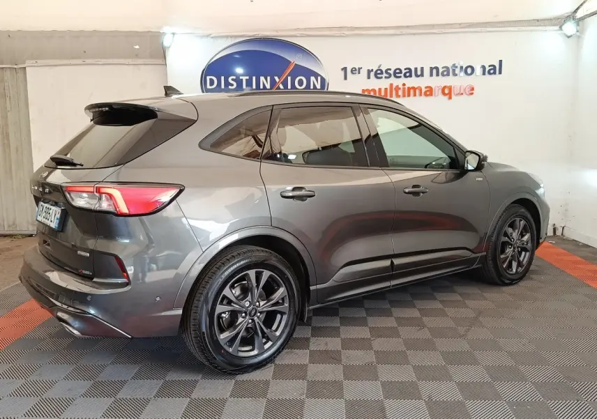 Ford Kuga gris foncé vu en 3/4 arrière droit, avec jantes noires et toit noir brillant dans un showroom.