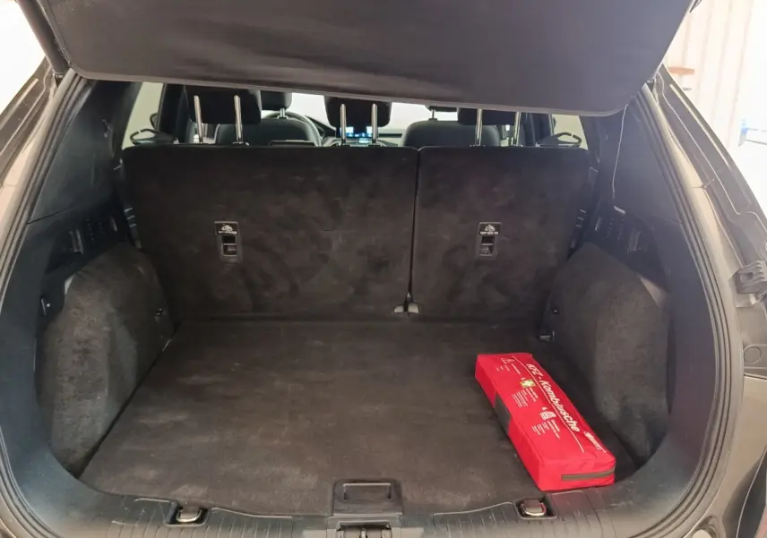 Coffre ouvert du Ford Kuga gris foncé vu de l'arrière, avec banquette arrière relevée et trousse de secours rouge.