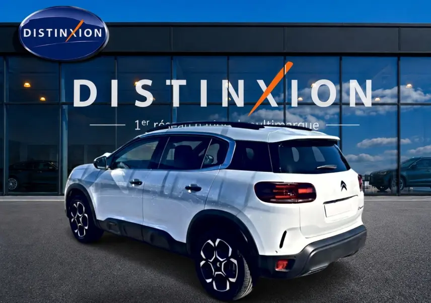Vue 3/4 arrière droite d'un Citroën C5 Aircross blanc avec jantes alu et barres de toit noires.