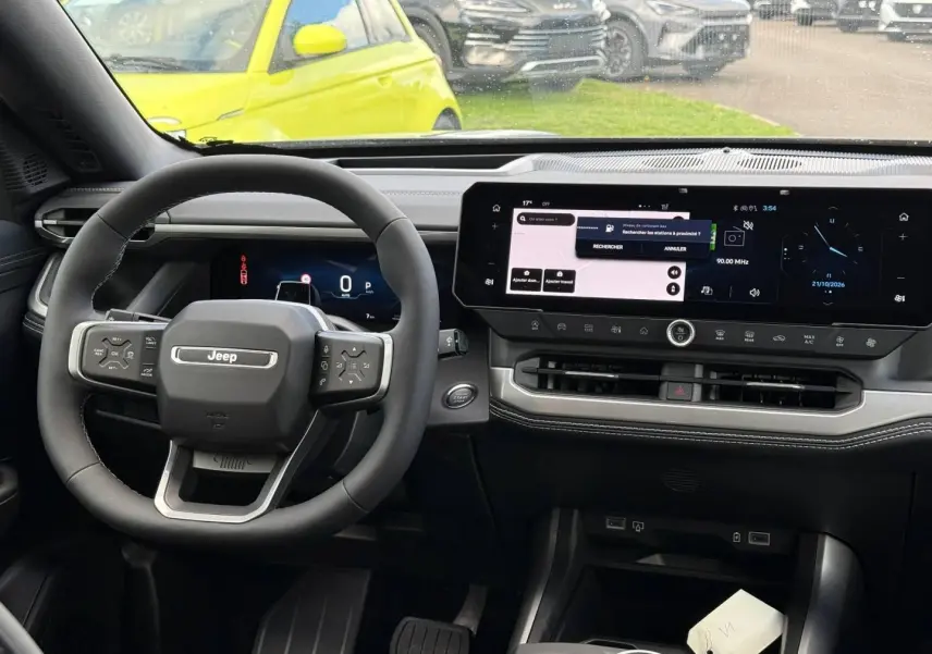Vue intérieure avant du Jeep Compass 2026, tableau de bord noir avec écran tactile panoramique et volant multifonctions.