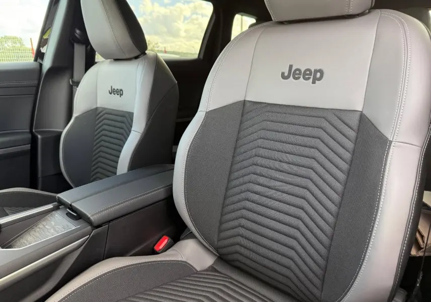 Gros plan sur les sièges avant gris clair et noir avec logo Jeep brodé, accoudoir central et intérieur lumineux.