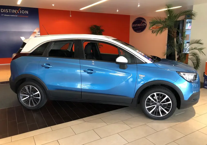Opel Crossland X bleu intens métal avec toit blanc, vue profil côté gauche en intérieur showroom.