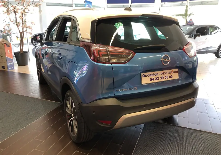 Vue 3/4 arrière gauche d'un Opel Crossland X bleu métallisé avec toit blanc en showroom.
