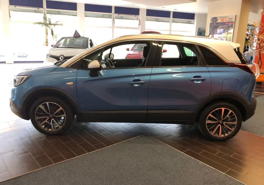 Opel Crossland X bleu intense métal en vue profil côté gauche, toit blanc contrasté et jantes alliage biton noir.