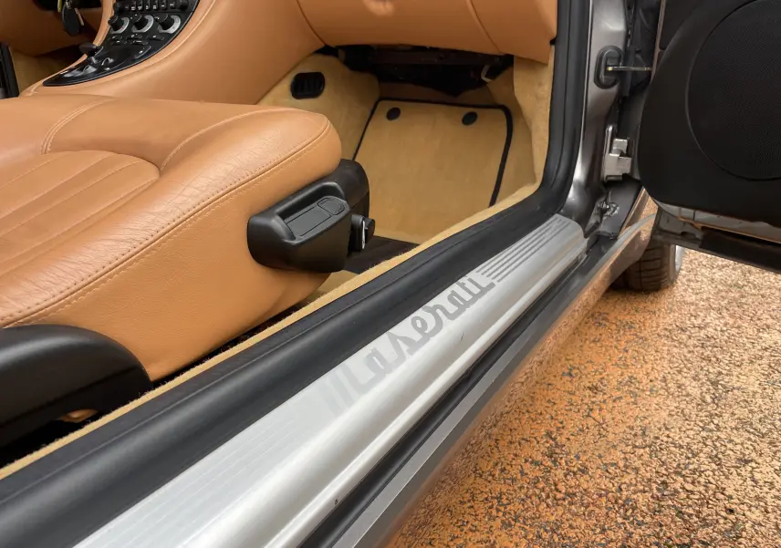 Vue rapprochée de l'entrée côté gauche d'une Maserati Spyder gris Nuvolari avec intérieur cuir beige et seuil marqué Maserati.
