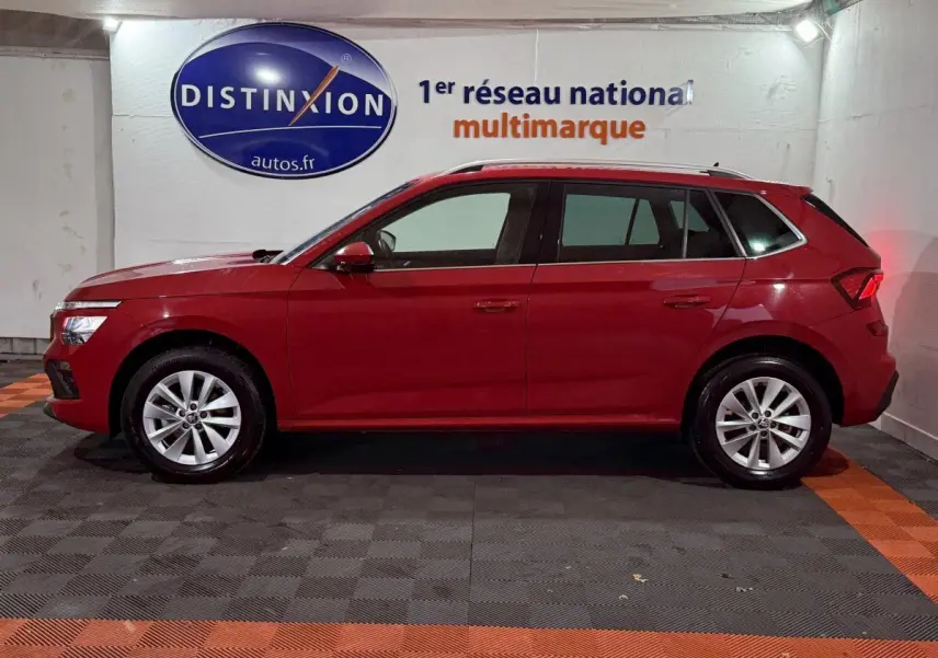 Profil latéral droit d'un SUV SKODA KAMIQ rouge 2024 dans un garage avec sol noir et orange.