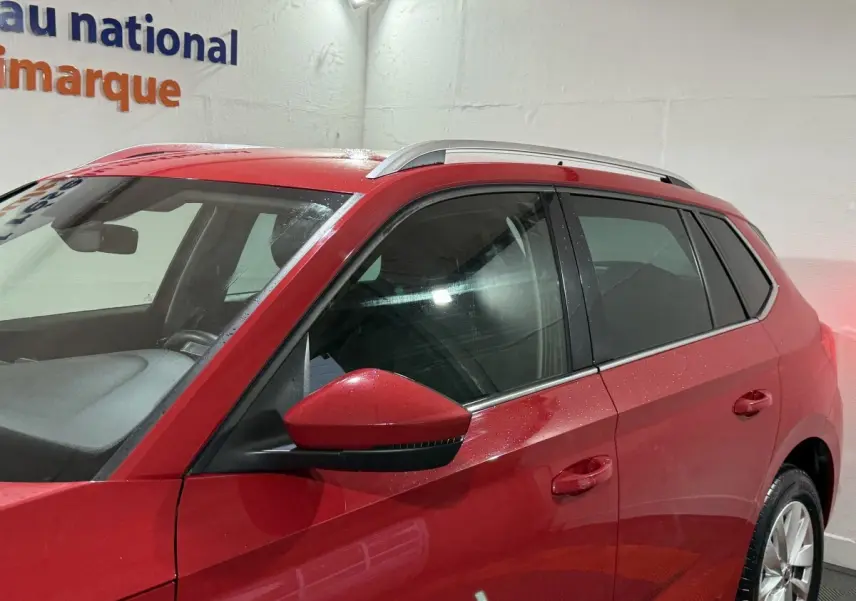 Vue de côté gauche du SKODA KAMIQ rouge 2024, mettant en valeur les vitres teintées et les barres de toit argentées.