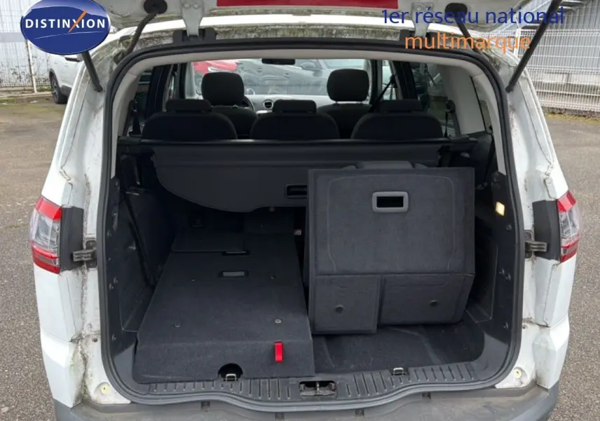 Vue arrière du coffre ouvert du Ford S-MAX blanc, montrant les sièges arrière partiellement rabattus et l'espace de chargement.