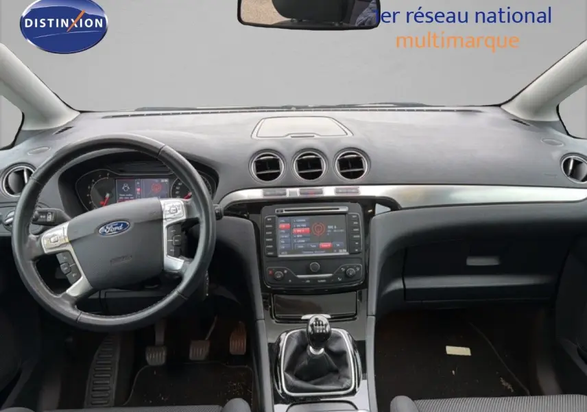 Vue intérieure frontale du tableau de bord et volant noir d’une Ford S-MAX blanche de 2013 avec boîte manuelle.