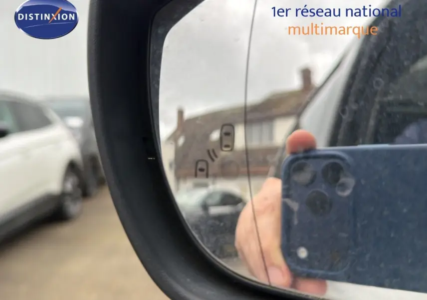 Rétroviseur extérieur gauche d’un Ford S-MAX blanc de 2013, avec reflet flou d’un bâtiment et d’un téléphone.