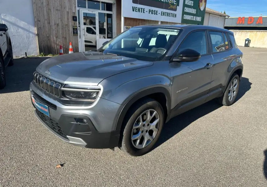 Jeep Avenger gris en 3/4 avant droit, avec jantes alliage 17 pouces et calandre distinctive sous un ciel bleu.