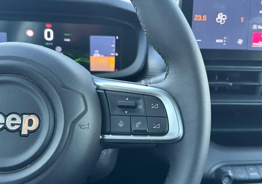 Gros plan sur le volant noir du Jeep Avenger gris 2025, avec commandes intégrées et tableau de bord numérique visible.