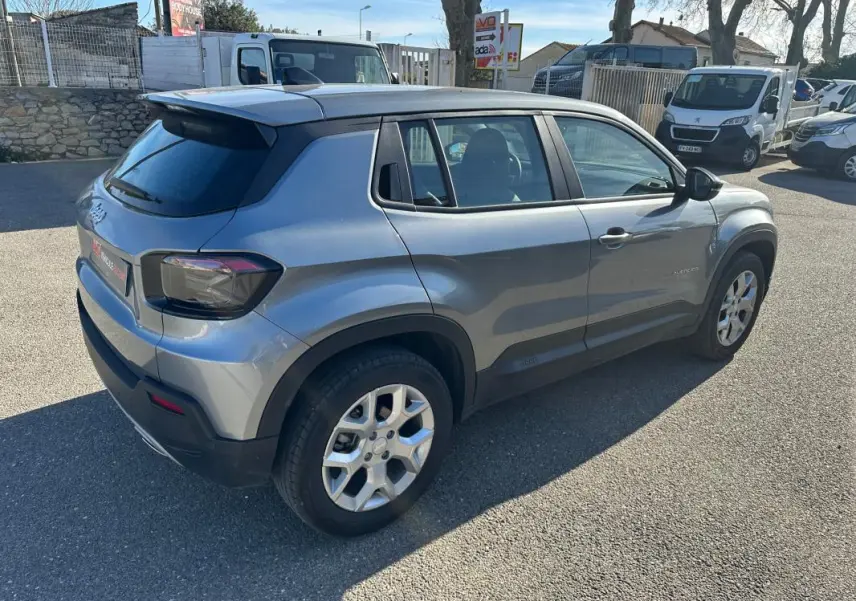 Jeep Avenger gris vue 3/4 arrière droit, jantes alliage 17 pouces et vitres teintées dans un parking extérieur.