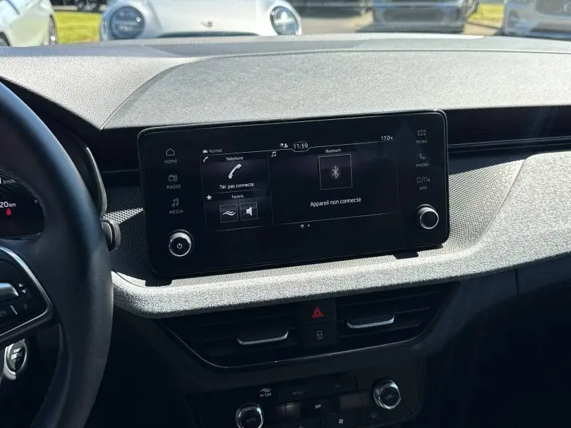 Vue intérieure centrée sur l'écran tactile du tableau de bord de la Skoda Scala bleu, avec volant partiellement visible à gauche.