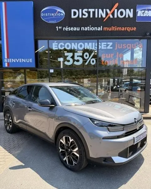 Vue 3/4 avant gauche d'une Citroën C4 gris foncé 2025 stationnée devant une vitrine avec enseigne Distinxion.