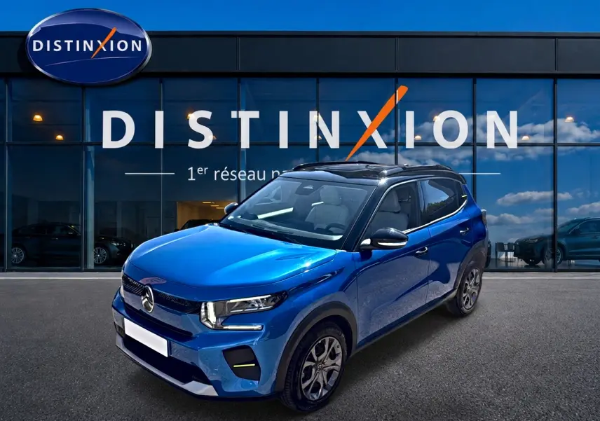 Vue 3/4 avant droite d'une Citroën C3 bleu 2025 avec toit noir et jantes alu devant un bâtiment Distinxion.
