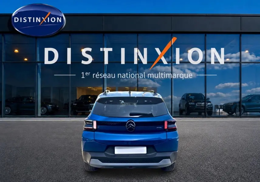Vue arrière d'une Citroën C3 bleu 2025 stationnée devant une vitrine avec logo Distinxion.
