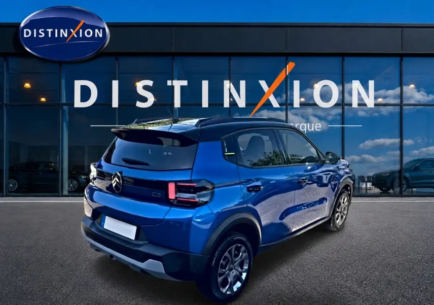 Vue 3/4 arrière droite d'une Citroën C3 bleue 2025 avec feux arrière LED et jantes alu devant un showroom Distinxion.