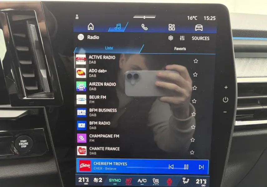 Écran central tactile du tableau de bord Renault Rafale 2025 affichant les stations radio, avec reflets et commandes autour.