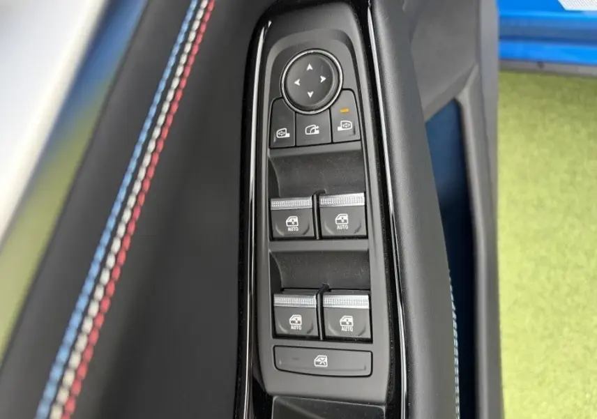 Gros plan sur les commandes de vitres et rétroviseurs avec surpiqûres tricolores sur la garniture intérieure bleu sommet.