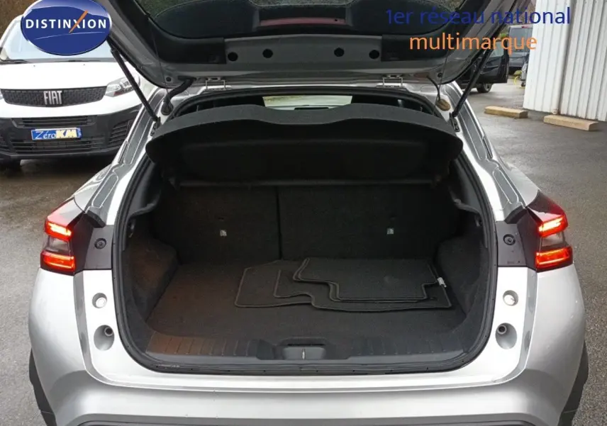 Vue arrière d'un Nissan Juke gris platine 2020 avec coffre ouvert et tapis de sol visibles, feux arrière allumés.