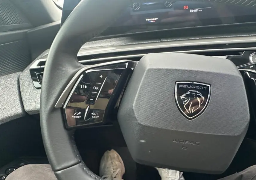 Vue rapprochée du volant cuir noir du Peugeot 3008 Hybrid 136 e-DCS6 Allure avec commandes intégrées et logo lion.