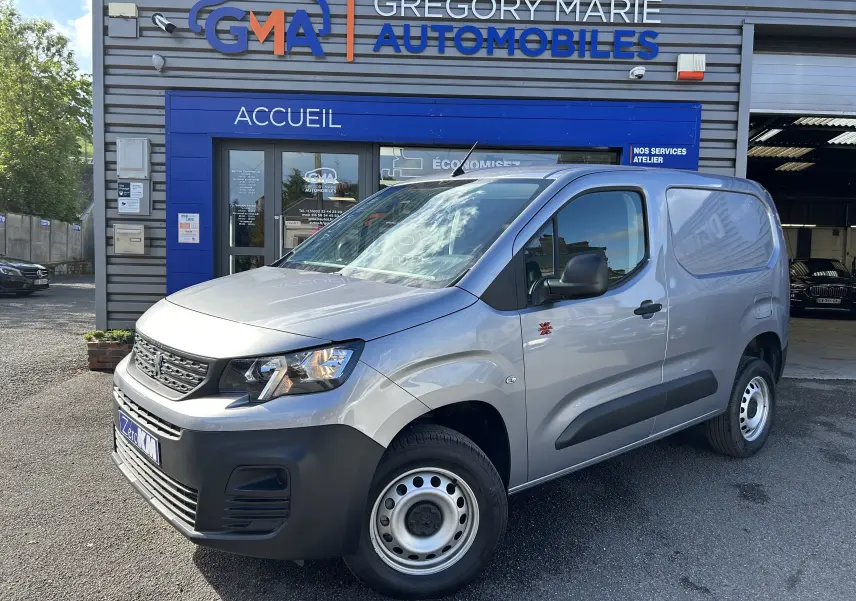 Vue 3/4 avant droit d'un Peugeot Partner Dangel 4x4 gris Artense avec protections noires et jantes acier devant un garage.