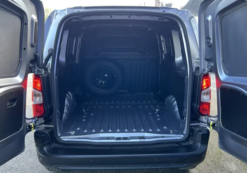 Vue arrière du Peugeot Partner Dangel gris Artense avec portes ouvertes, montrant l'espace de chargement vide et une roue de secours fixée à l'intérieur.