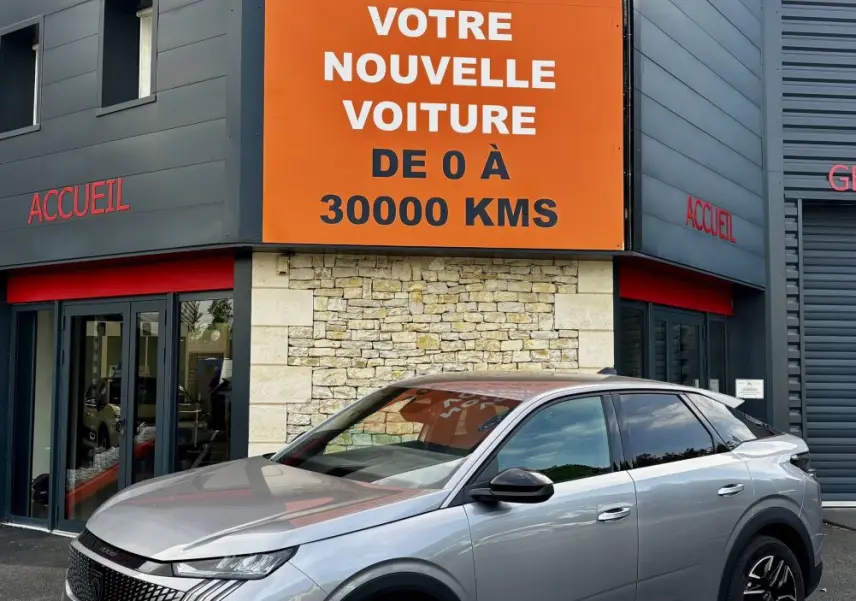 Peugeot 3008 gris clair vue 3/4 avant droit, avec calandre distinctive et jantes noires, devant un bâtiment commercial.