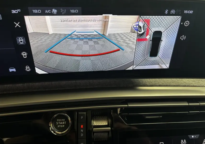 Vue intérieure du tableau de bord du Peugeot 3008 gris clair 2025, avec écran de caméra de recul et bouton démarrage visible.