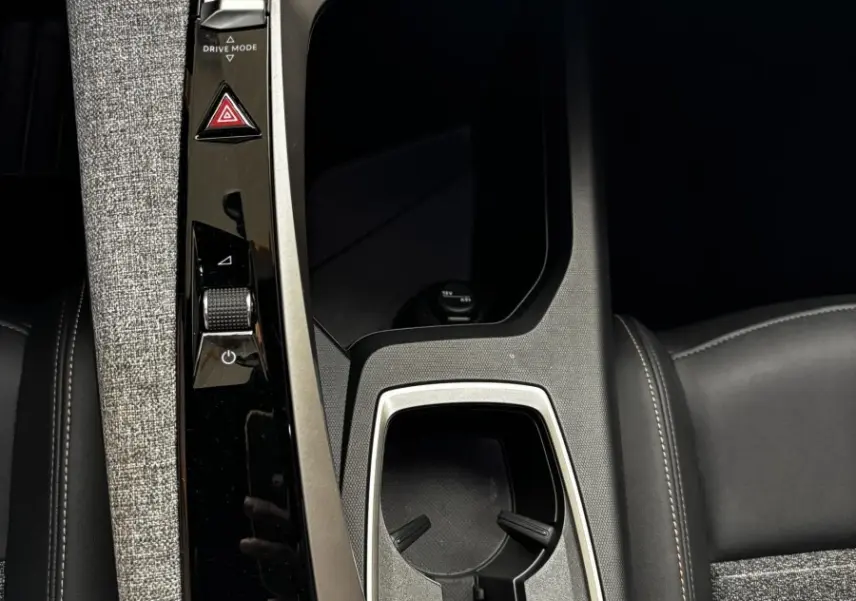 Vue rapprochée de la console centrale noire et grise du Peugeot 3008 1.2 Hybrid 145 Allure avec porte-gobelets et commandes tactiles.