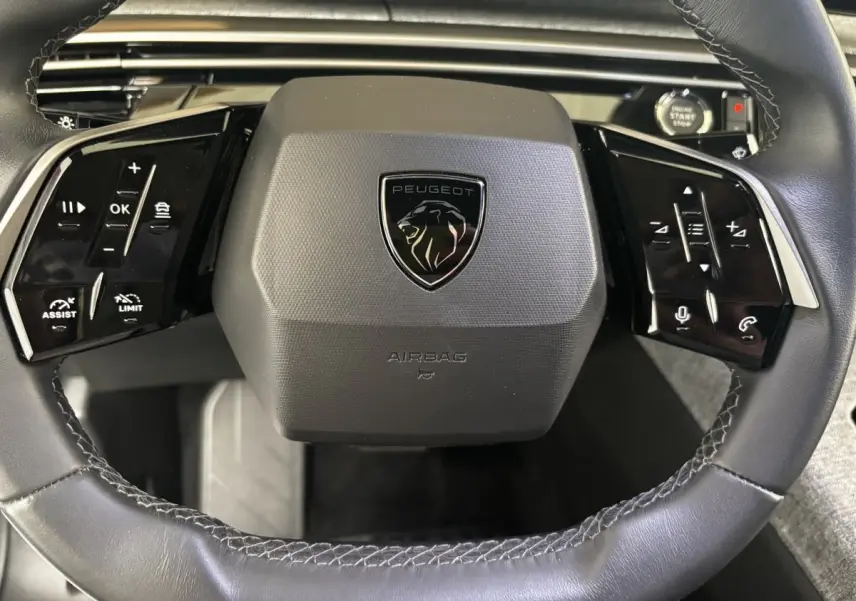 Gros plan sur le volant cuir noir du Peugeot 3008 2025 avec commandes multifonctions et bouton démarrage visible.