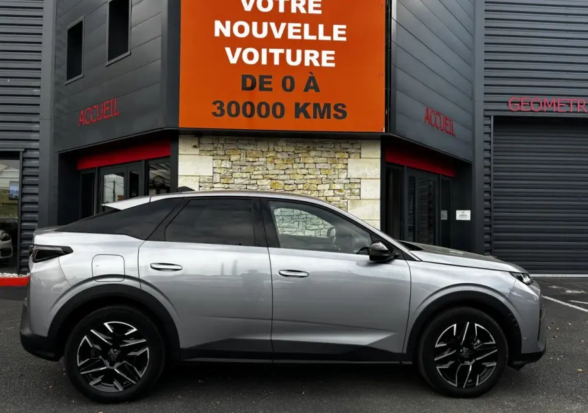 Peugeot 3008 hybride gris clair vue de profil côté gauche, roues noires à jantes stylisées, stationnée devant un bâtiment.