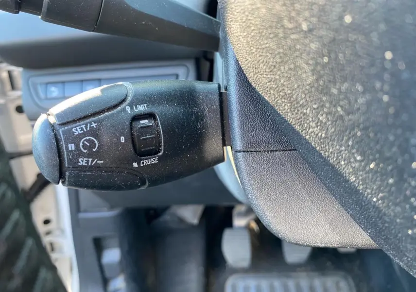 Gros plan sur la commande de régulateur de vitesse à gauche du volant dans une Peugeot 208 blanche de 2019.