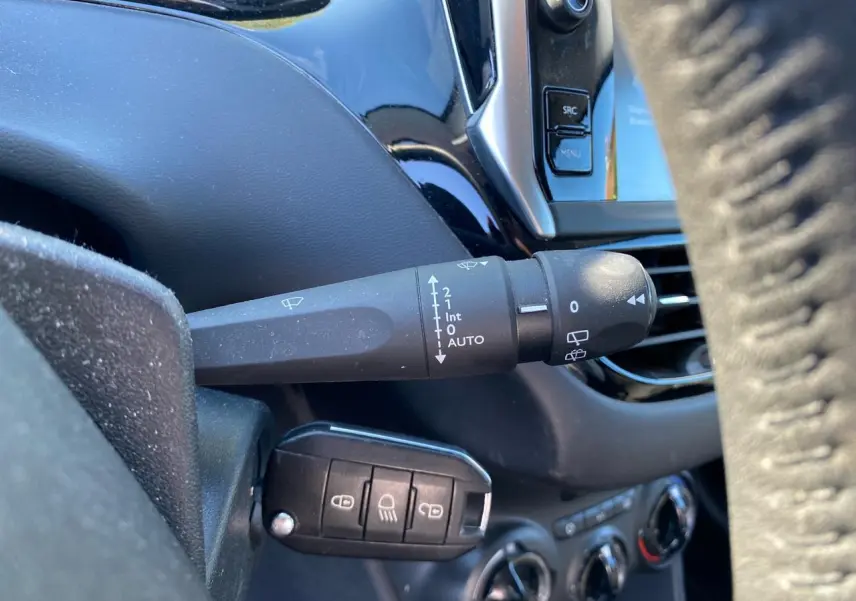 Gros plan sur la commande d’essuie-glace et la clé de contact dans l’habitacle d’une Peugeot 208 blanche de 2019.
