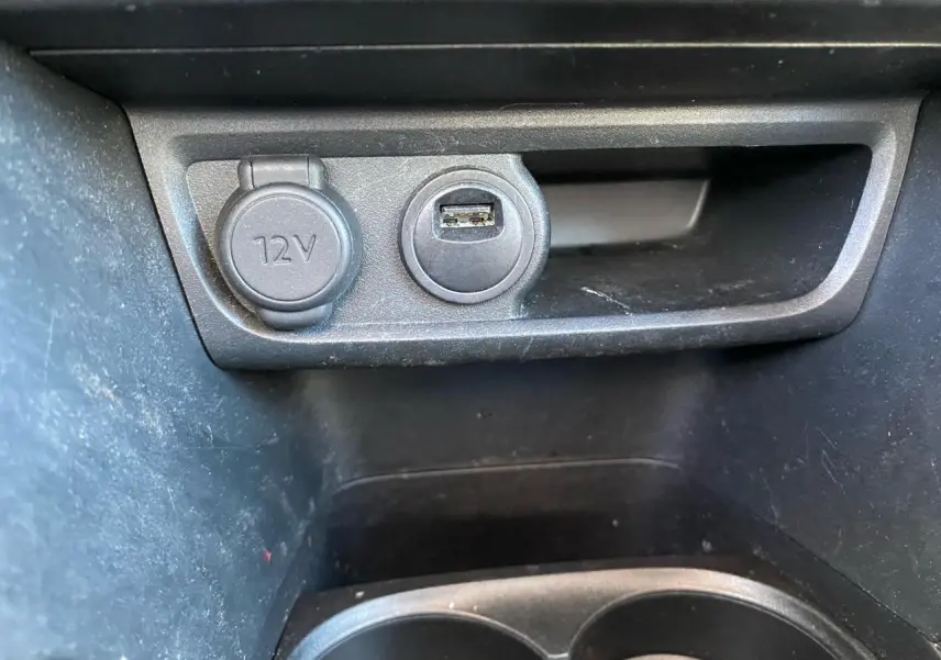 Gros plan sur la prise 12V et port USB dans l’espace de rangement intérieur noir d’une Peugeot 208 blanche.